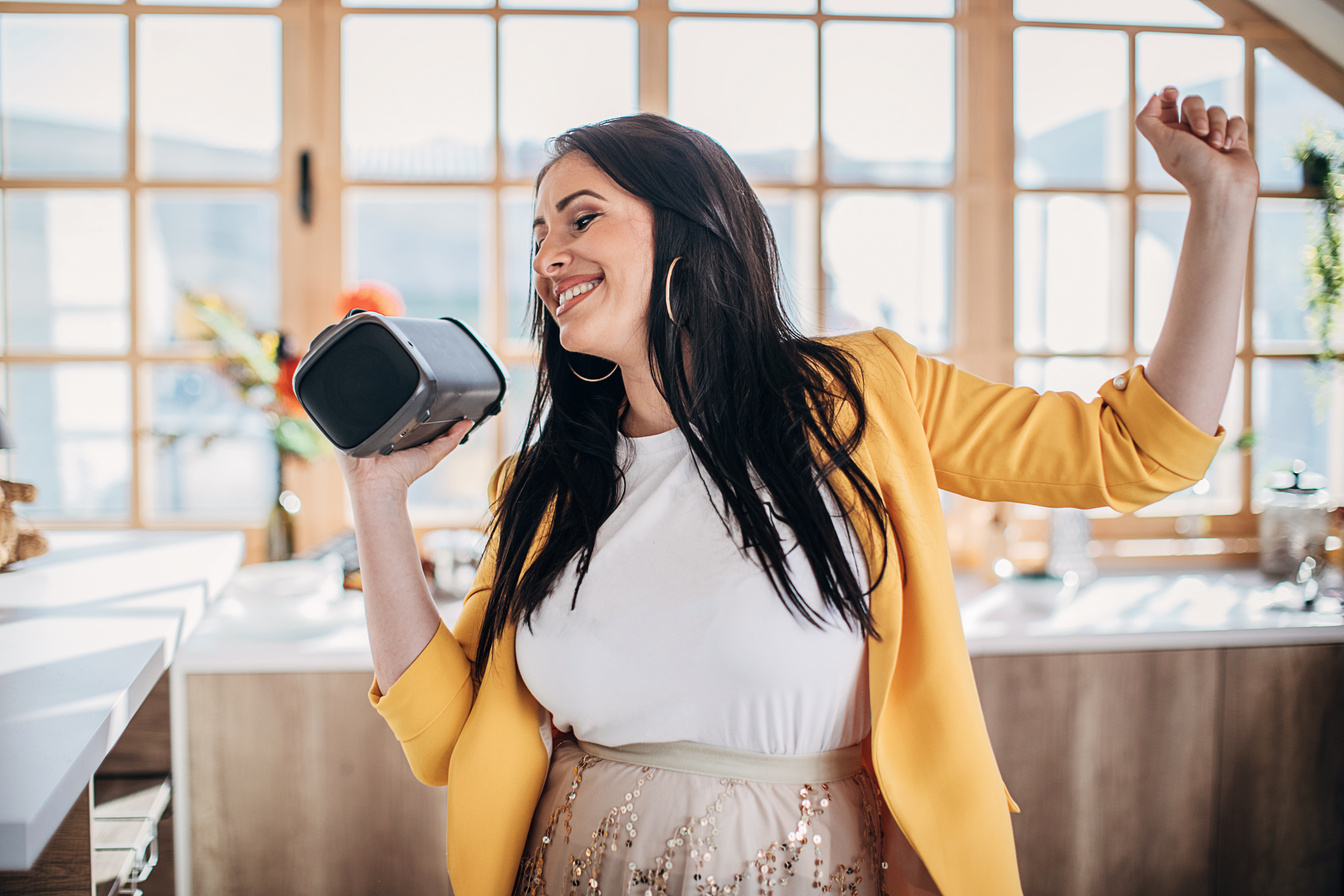 Woman singing and dancing at home and holding wireless bluetooth speaker